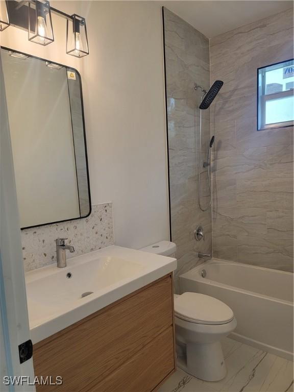 full bathroom with tiled shower / bath, vanity, and toilet