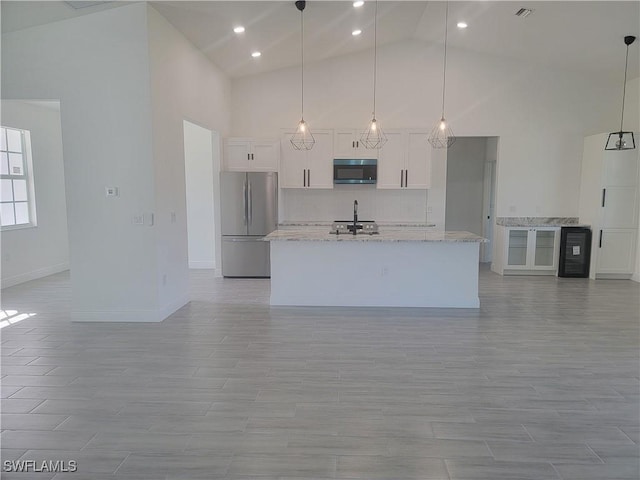 kitchen featuring hanging light fixtures, light stone countertops, white cabinets, and freestanding refrigerator