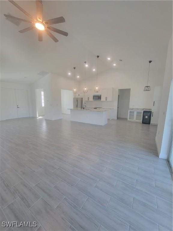 unfurnished living room featuring a ceiling fan, a sink, and high vaulted ceiling