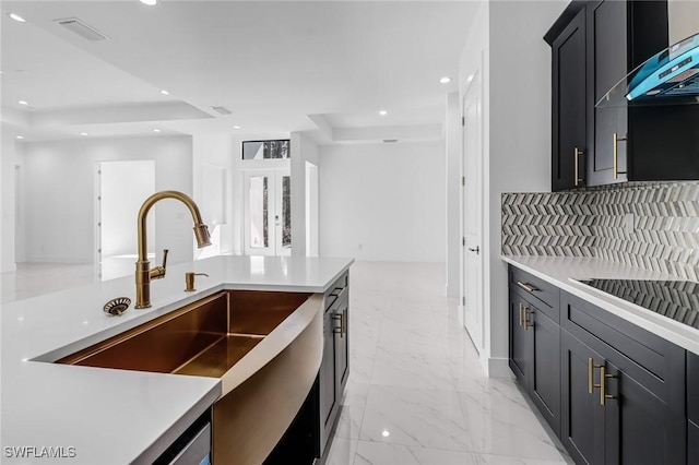 kitchen featuring sink, a tray ceiling, and wall chimney range hood