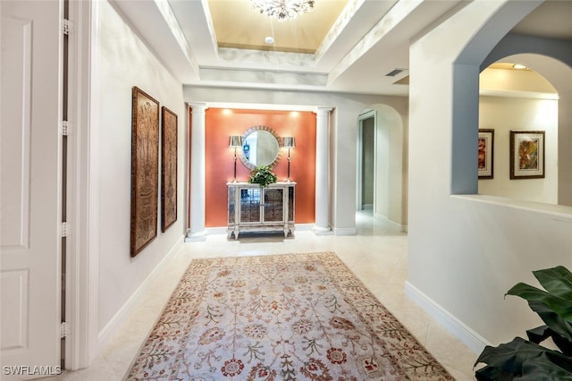 hall with a raised ceiling, ornamental molding, and ornate columns