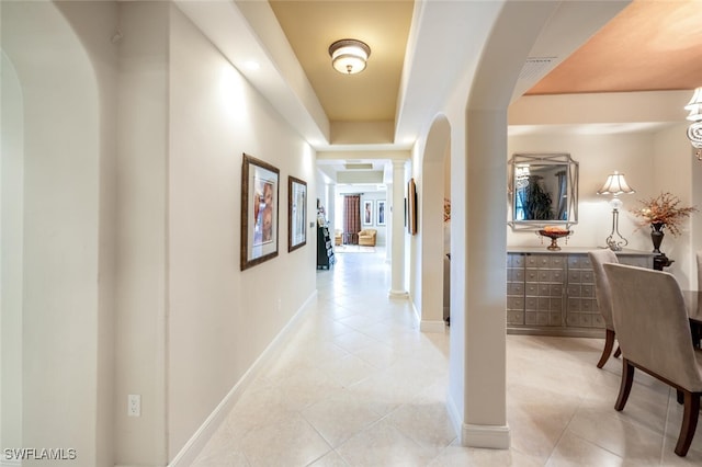 corridor featuring light tile patterned floors and a tray ceiling