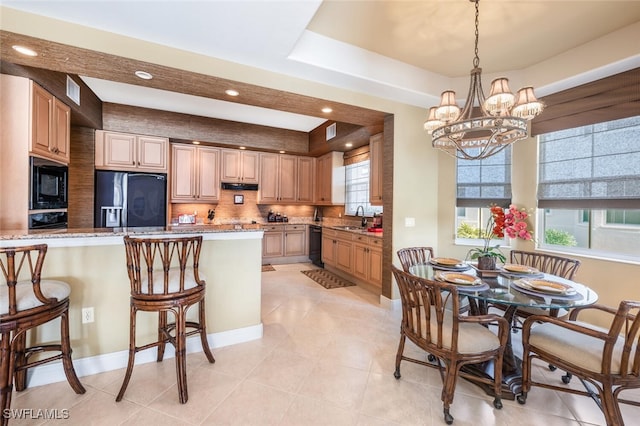 kitchen with light stone countertops, a raised ceiling, sink, black appliances, and a notable chandelier