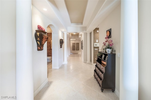 hallway with light tile patterned flooring and a tray ceiling