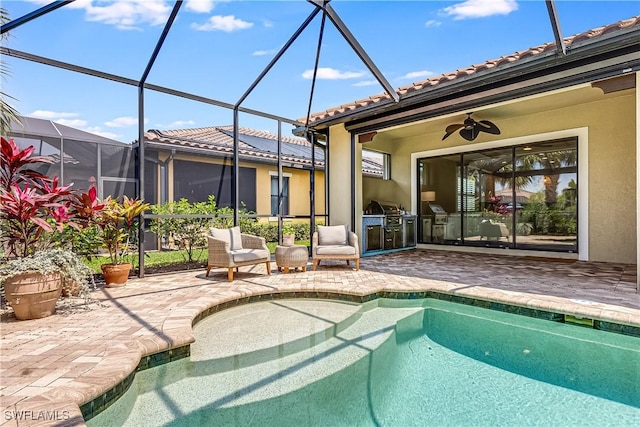 view of swimming pool featuring a patio, glass enclosure, ceiling fan, and exterior kitchen