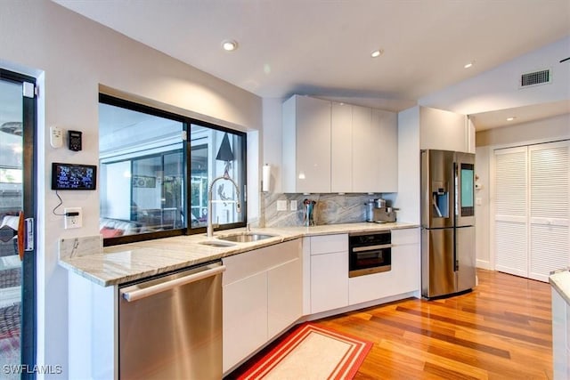 kitchen featuring appliances with stainless steel finishes, tasteful backsplash, sink, white cabinetry, and lofted ceiling