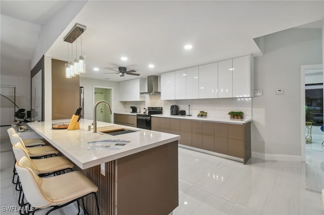 kitchen with black / electric stove, wall chimney range hood, sink, white cabinets, and hanging light fixtures