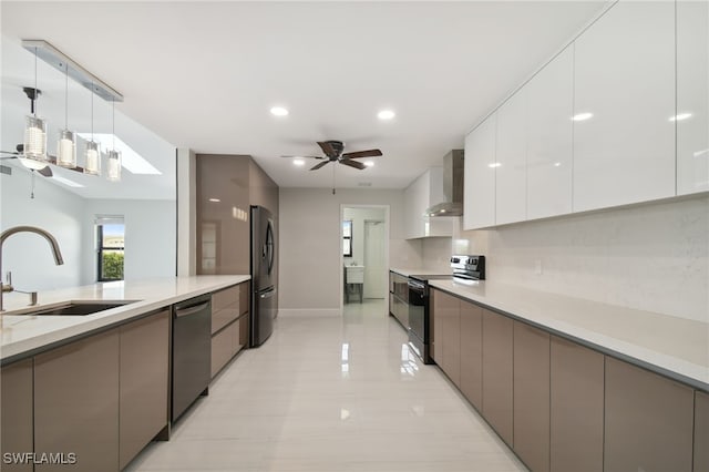 kitchen featuring pendant lighting, white cabinets, wall chimney range hood, sink, and stainless steel appliances