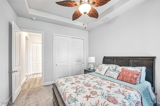 bedroom with light carpet, a closet, ceiling fan, and a tray ceiling