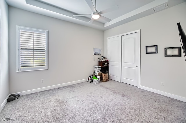 unfurnished bedroom with carpet flooring, ceiling fan, a raised ceiling, and a closet