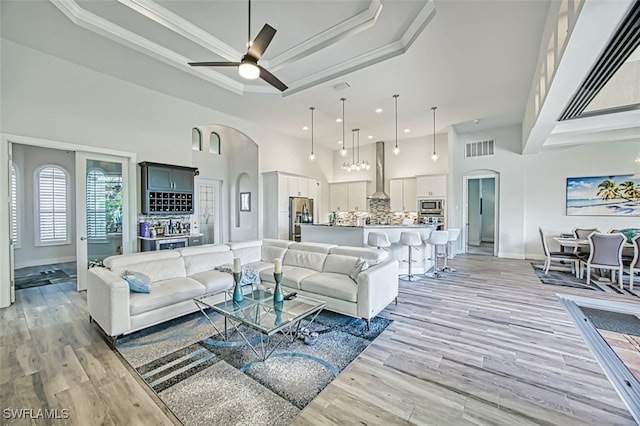 living room featuring a raised ceiling, ceiling fan, ornamental molding, a towering ceiling, and light hardwood / wood-style floors