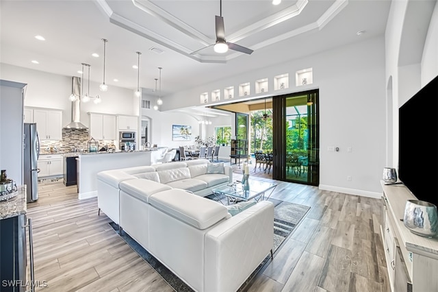 living room with a raised ceiling, ceiling fan, and crown molding