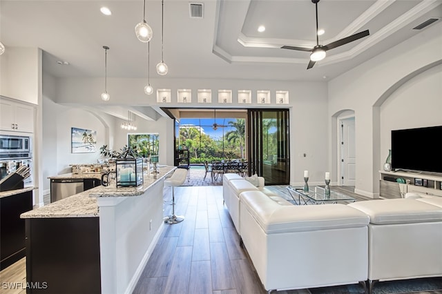 living room featuring hardwood / wood-style floors, ceiling fan with notable chandelier, a raised ceiling, and crown molding