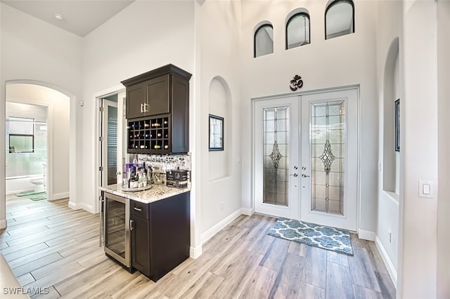 bar with french doors, beverage cooler, dark brown cabinets, and light hardwood / wood-style floors