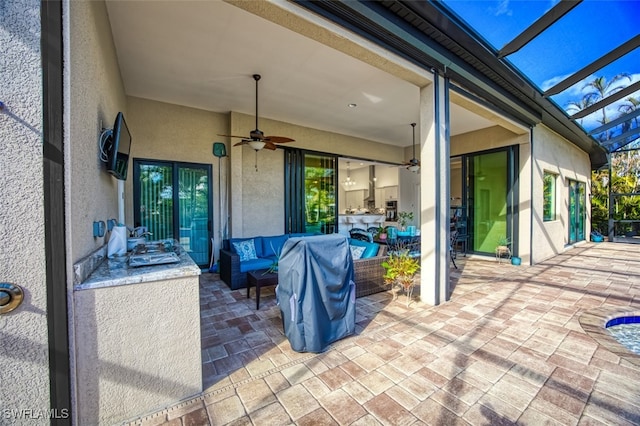 view of patio featuring ceiling fan, an outdoor hangout area, and glass enclosure