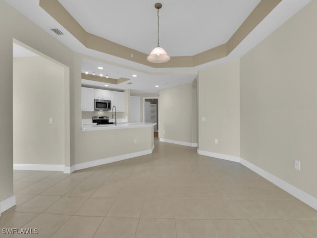 unfurnished living room with sink, a tray ceiling, and light tile patterned flooring