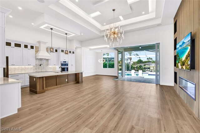 unfurnished living room featuring light hardwood / wood-style flooring, a raised ceiling, a notable chandelier, and sink