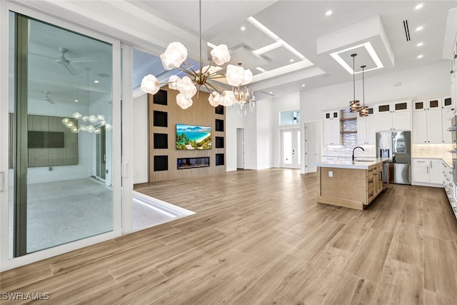 kitchen with a center island with sink, white cabinets, stainless steel fridge, a towering ceiling, and decorative light fixtures