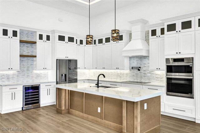 kitchen with wine cooler, hanging light fixtures, custom exhaust hood, and an island with sink