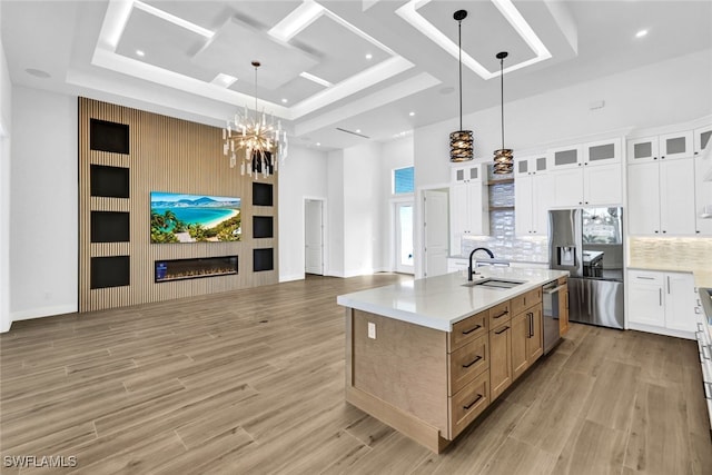 kitchen featuring a large island with sink, sink, appliances with stainless steel finishes, decorative light fixtures, and white cabinetry