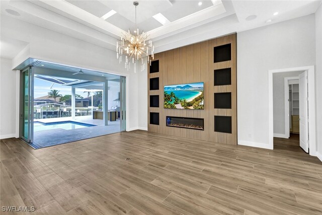 unfurnished living room with hardwood / wood-style floors, wooden walls, a towering ceiling, a large fireplace, and a chandelier