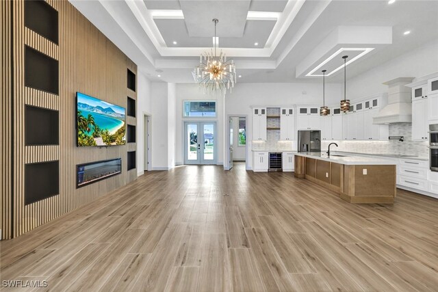 kitchen with a high ceiling, a large island with sink, decorative light fixtures, white cabinets, and custom exhaust hood