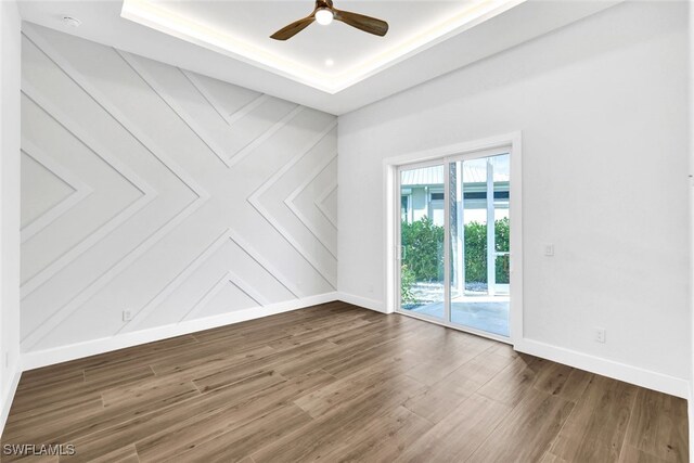 empty room featuring a tray ceiling, ceiling fan, and dark hardwood / wood-style floors