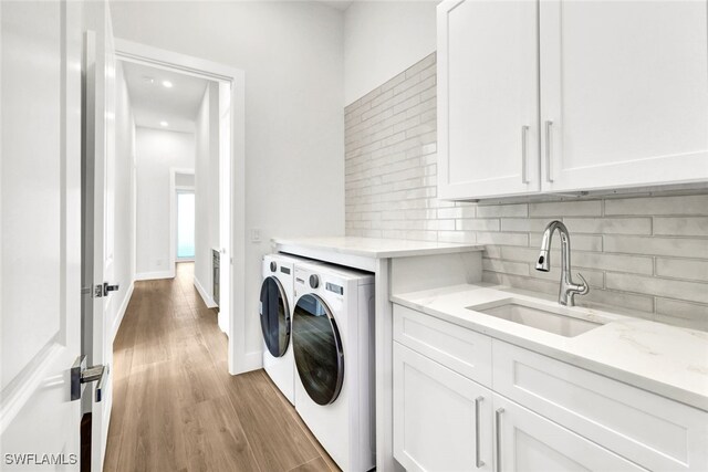 laundry area featuring separate washer and dryer, sink, cabinets, and wood-type flooring