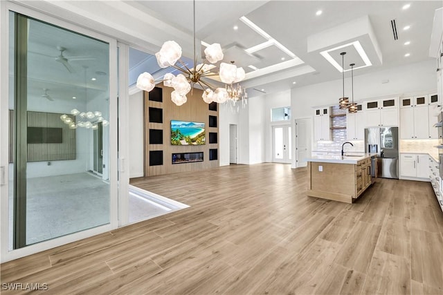 kitchen featuring a fireplace, stainless steel refrigerator with ice dispenser, light countertops, a high ceiling, and a sink