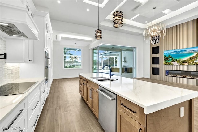 kitchen featuring a notable chandelier, appliances with stainless steel finishes, a kitchen island with sink, a sink, and premium range hood