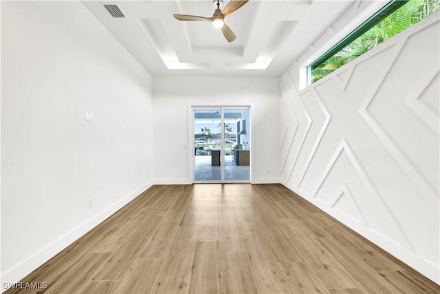 spare room featuring light wood-type flooring, a tray ceiling, visible vents, and baseboards