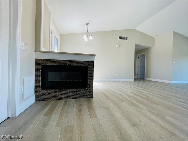 unfurnished living room with a tile fireplace, light hardwood / wood-style floors, lofted ceiling, and an inviting chandelier