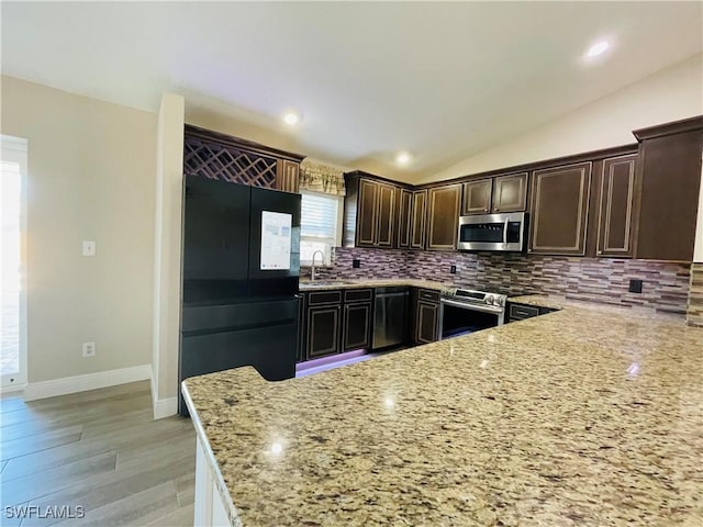 kitchen with light stone countertops, sink, backsplash, lofted ceiling, and appliances with stainless steel finishes