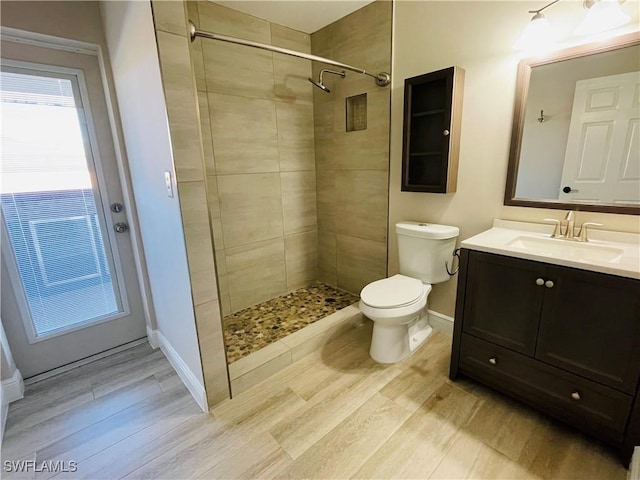 bathroom featuring a tile shower, vanity, toilet, and hardwood / wood-style floors