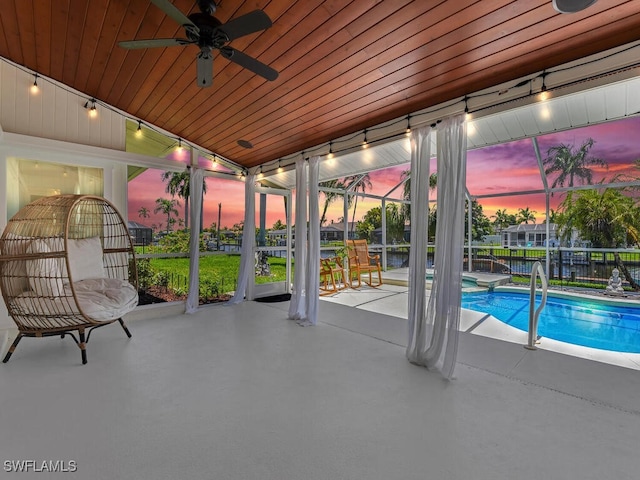 pool at dusk with a lanai, a patio area, and ceiling fan