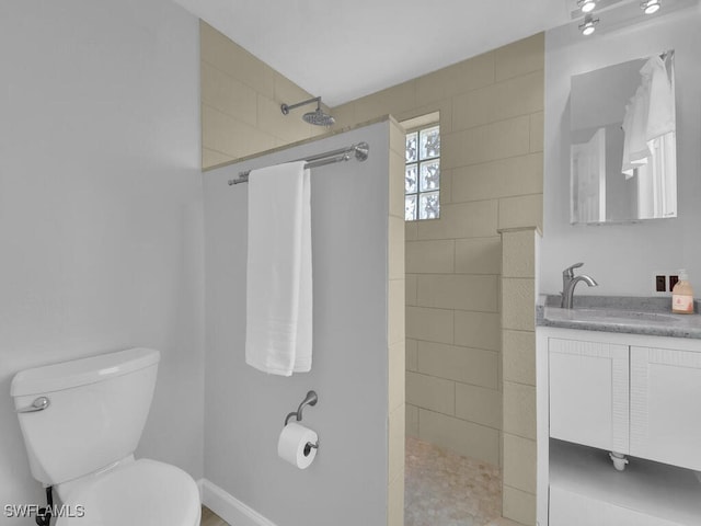 bathroom featuring a tile shower, vanity, and toilet