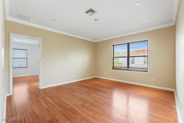 spare room with light wood-style floors, crown molding, a wealth of natural light, and visible vents