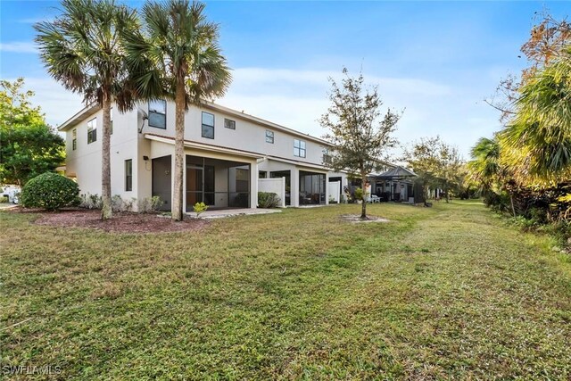 rear view of property featuring a sunroom, a lawn, and stucco siding