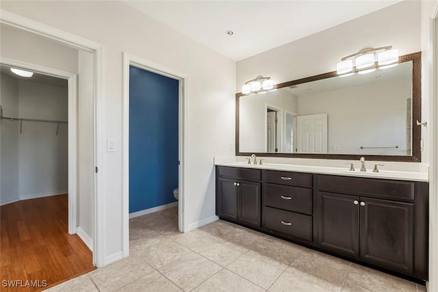 bathroom with double vanity, a sink, toilet, and baseboards