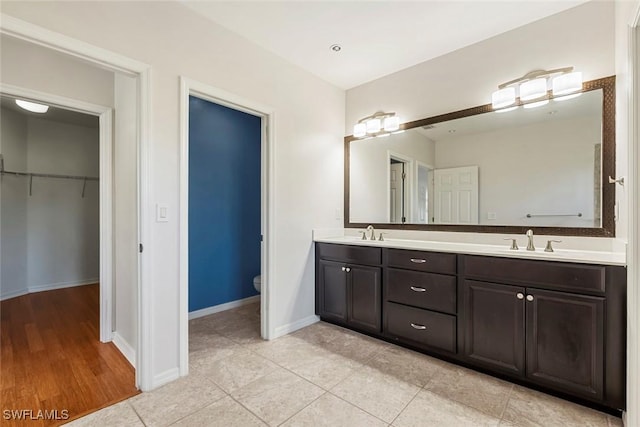 full bathroom featuring double vanity, toilet, baseboards, and a sink