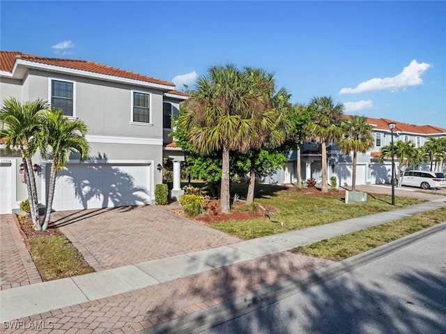 view of front of house with decorative driveway, a tile roof, stucco siding, a garage, and a front lawn