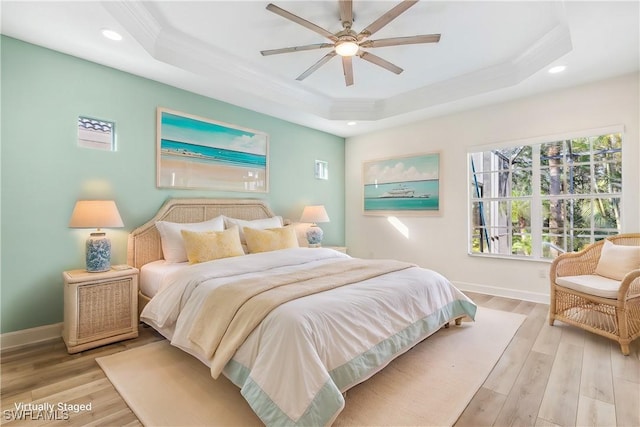 bedroom with a raised ceiling, ceiling fan, ornamental molding, and light wood-type flooring