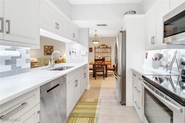 kitchen with appliances with stainless steel finishes, decorative light fixtures, white cabinetry, and sink