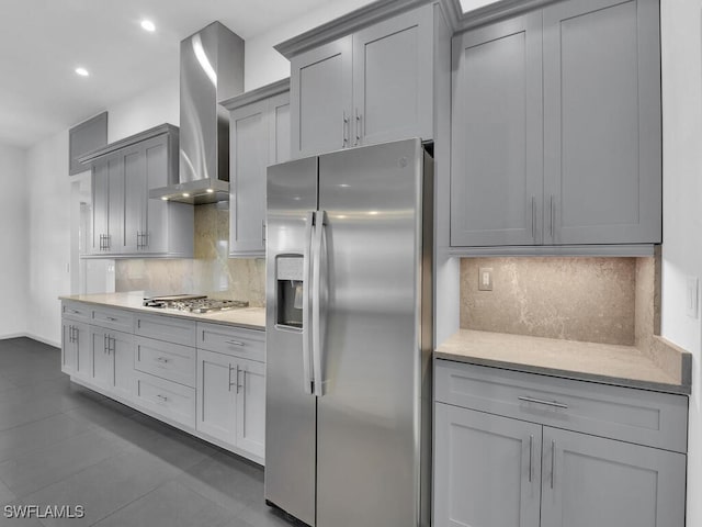 kitchen featuring gray cabinetry, dark tile patterned flooring, backsplash, stainless steel appliances, and wall chimney exhaust hood