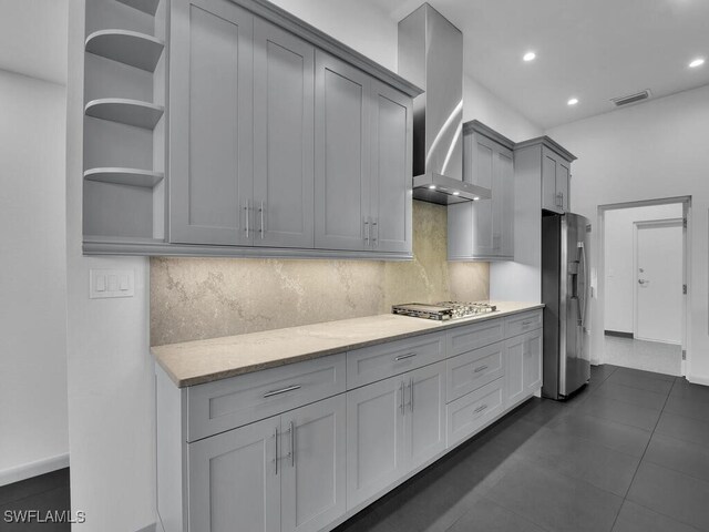 kitchen featuring tasteful backsplash, gray cabinetry, light stone counters, stainless steel appliances, and wall chimney range hood