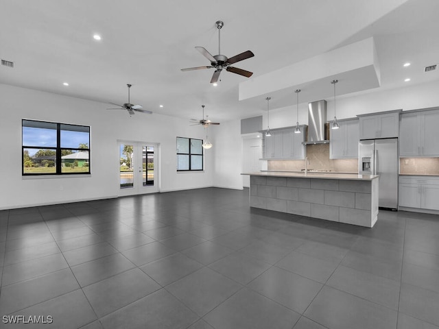 kitchen featuring tasteful backsplash, stainless steel fridge, hanging light fixtures, a large island, and wall chimney exhaust hood