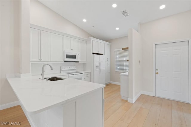 kitchen with a peninsula, white appliances, a sink, white cabinets, and light wood finished floors