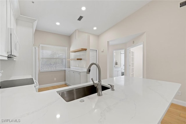 kitchen with white cabinetry, sink, light stone counters, kitchen peninsula, and light wood-type flooring