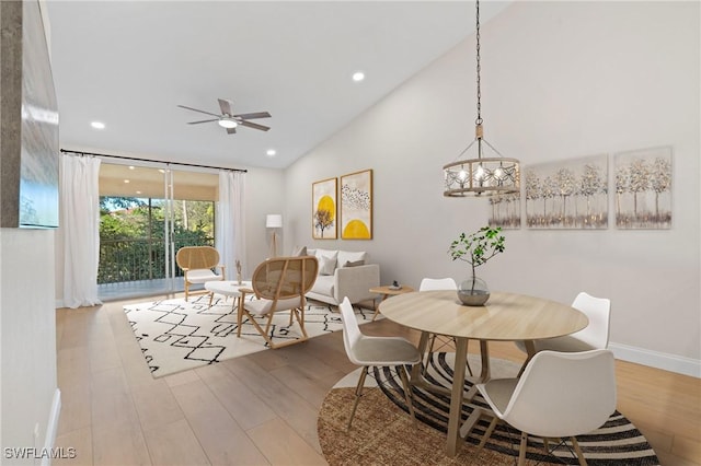 dining area with ceiling fan with notable chandelier, lofted ceiling, and light hardwood / wood-style flooring