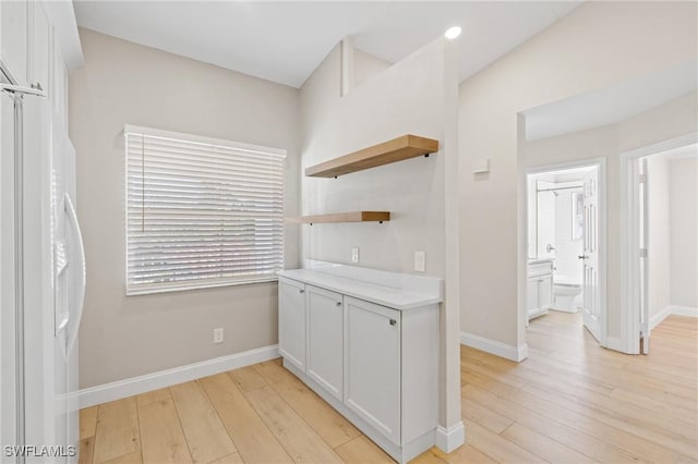 kitchen with light wood-style flooring, open shelves, white cabinetry, light countertops, and white fridge with ice dispenser